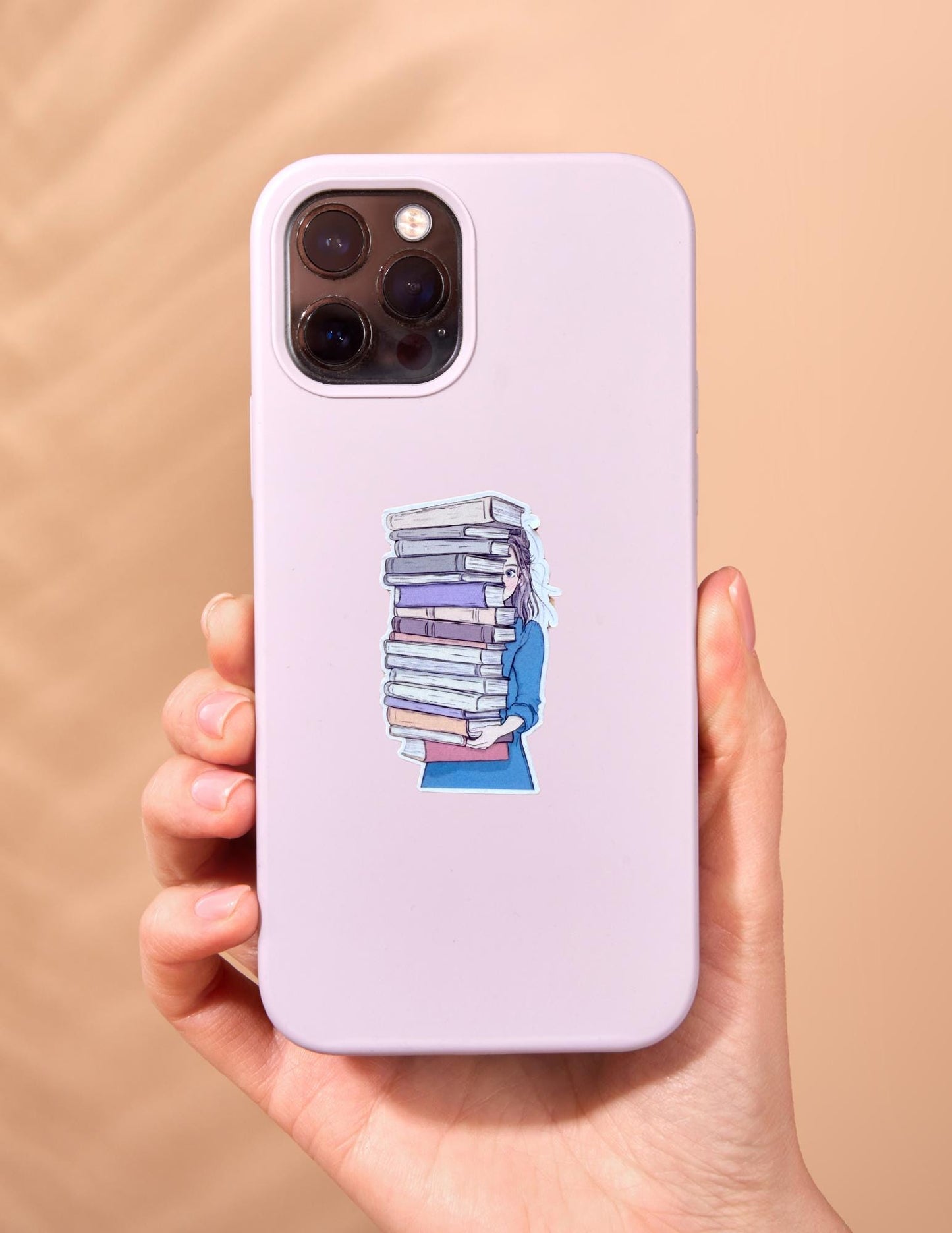 Vinyl sticker of a stacked pile of books in blue and beige tones, shown on the back of a white phone case. Perfect for bookworms, students, and literary lovers. __etsy:6907406839