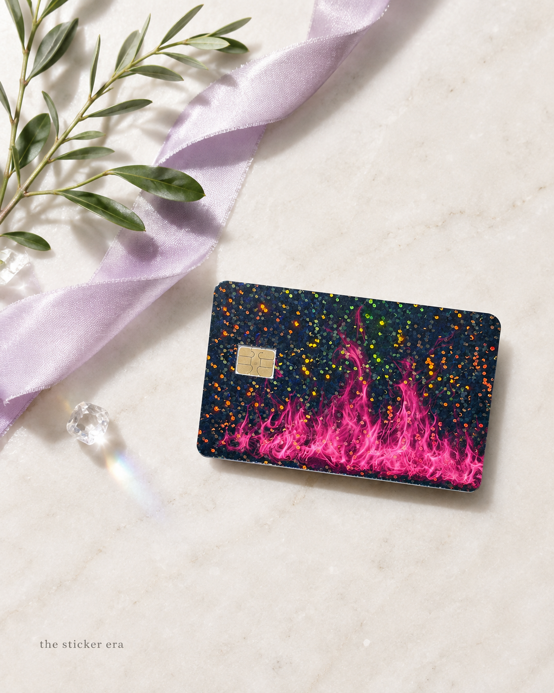Hot pink flame card skin with holographic glitter on a debit card beside lavender ribbon and olive leaves by The Sticker Era