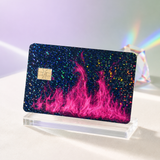 Holographic glitter pink fire credit card skin catching rainbow light on a clear stand by The Sticker Era