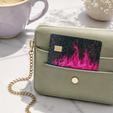 Hot pink flame debit card skin tucked into a sage green wallet next to a cup of coffee by The Sticker Era