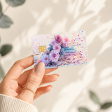  Hand holding a pastel floral book card skin against a white wall with soft leaf shadows by The Sticker Era