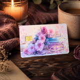 Pastel floral book card skin propped against a lit candle with a mug and an open book on dark wood by The Sticker Era