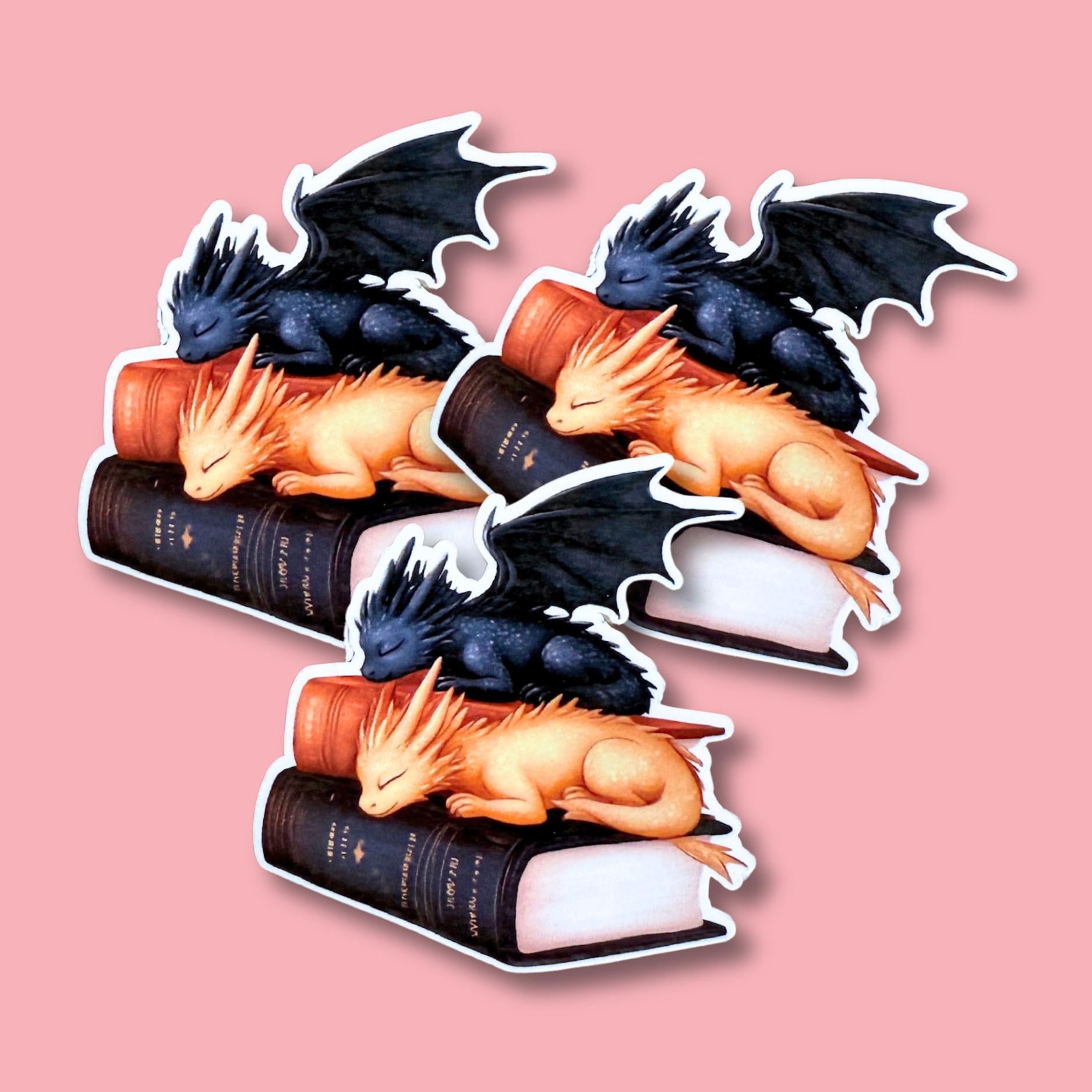 Sleeping black and gold dragons on stacked books vinyl sticker on pink background __etsy:7729911692
