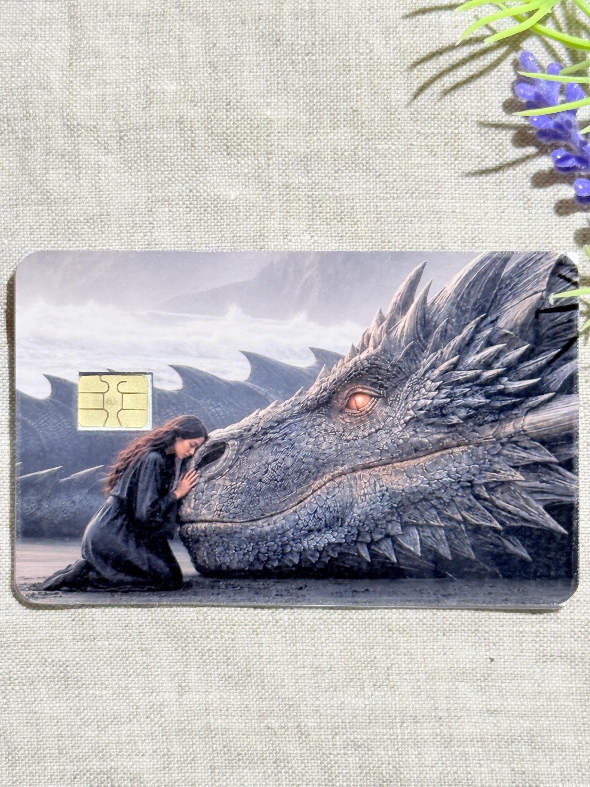 a debit card skin of a black dragon laying it's head down so a small woman may rest her head on his nose.
thestickerera __etsy:8156721827