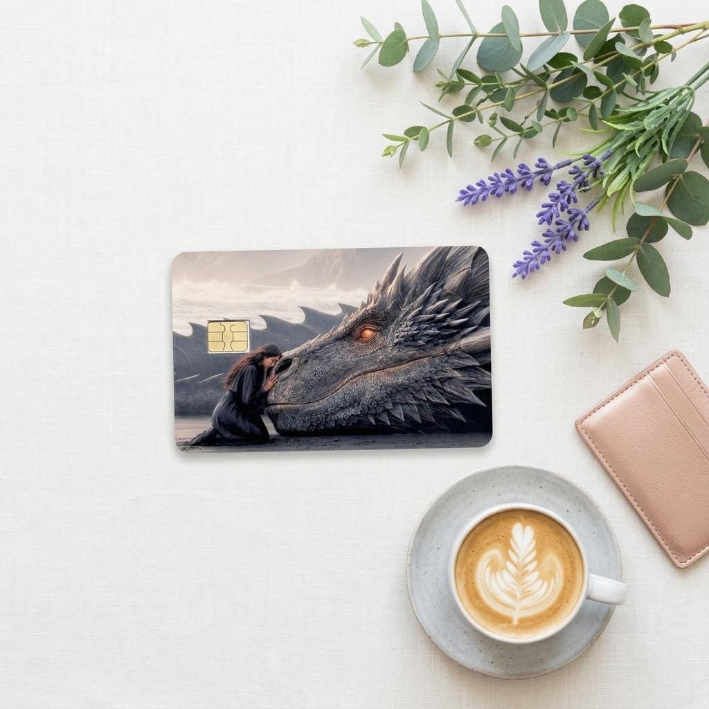 a debit card skin of a black dragon laying it's head down so a human can rest her head on the dragon on a cream colored cloth, flower and a hot coffee
 made by thestickerera __etsy:8156746597