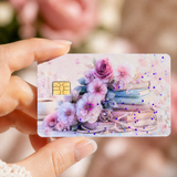 Hand holding up a pastel floral book card skin with blurred pink peonies behind it by The Sticker Era