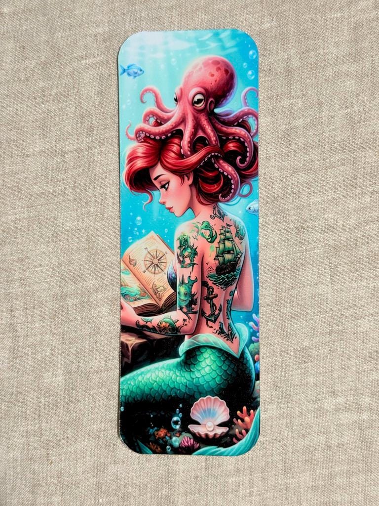 mermaid bookmark showing back of mermaid and side of face with her red hair and octopus n her head while she is reading, and a open clam with a pearl behind her. Bright blue ocean water in the background. __etsy:8125587880