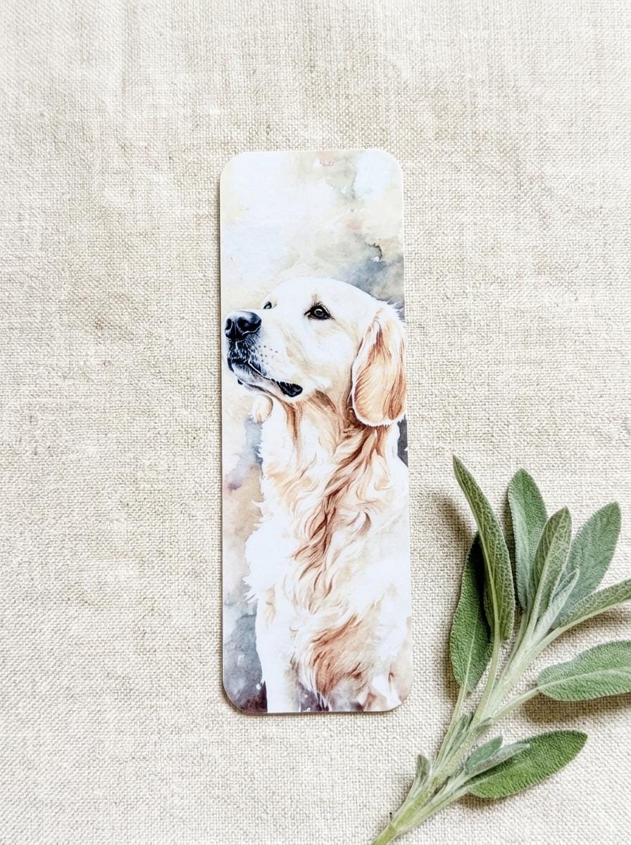 Close-up of a single English Cream Golden Retriever watercolor bookmark on a beige linen background, with a sprig of green sage beside it. __etsy:8181669877