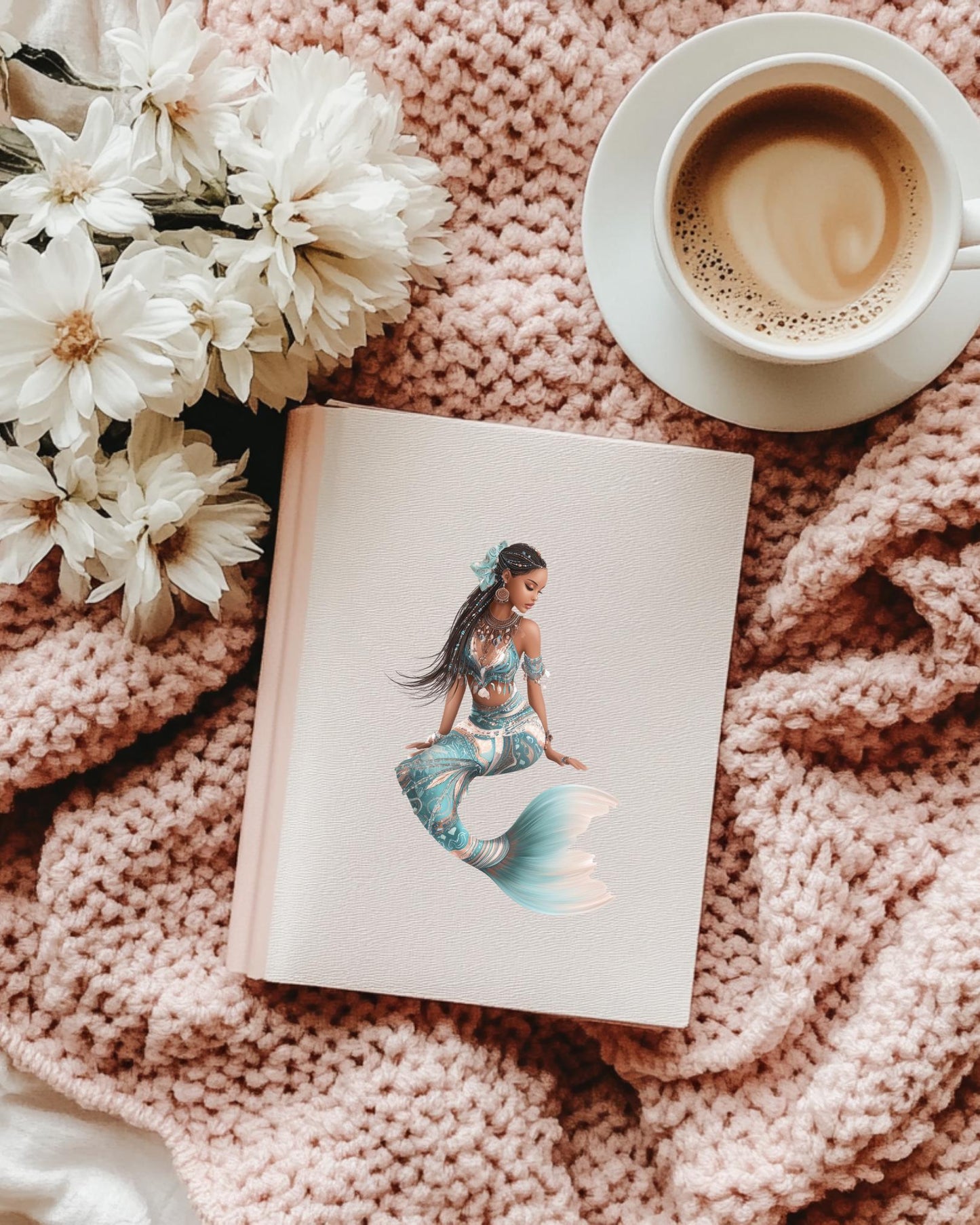 A cream journal decorated with the Ethiopian mermaid sticker, resting on a soft pink knitted blanket with white flowers and a cup of coffee. __etsy:7725789949