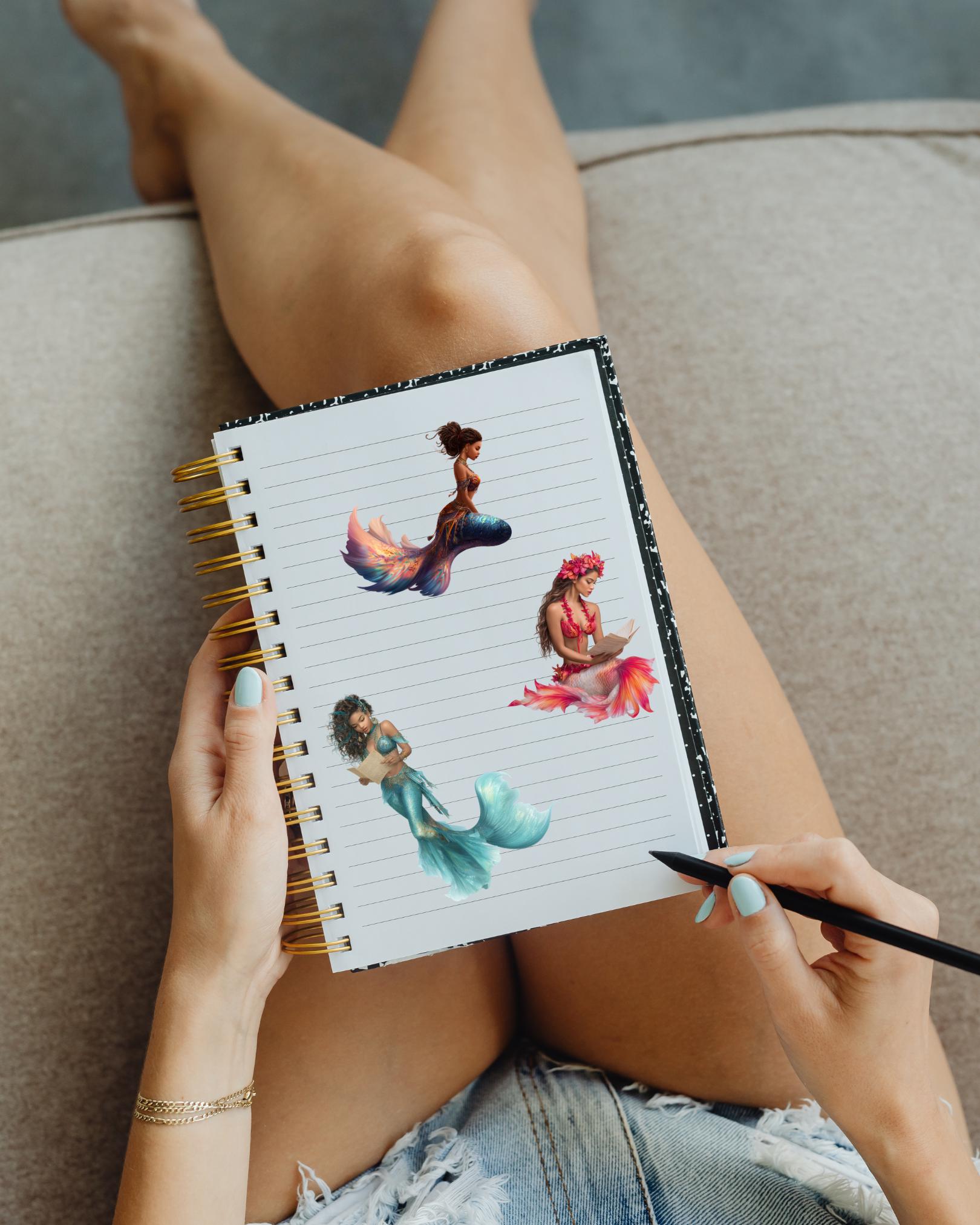 A person holding a spiral notebook on their lap, its cover decorated with the Ethiopian mermaid sticker and other mermaid stickers, with a pen in hand. __etsy:7677848218