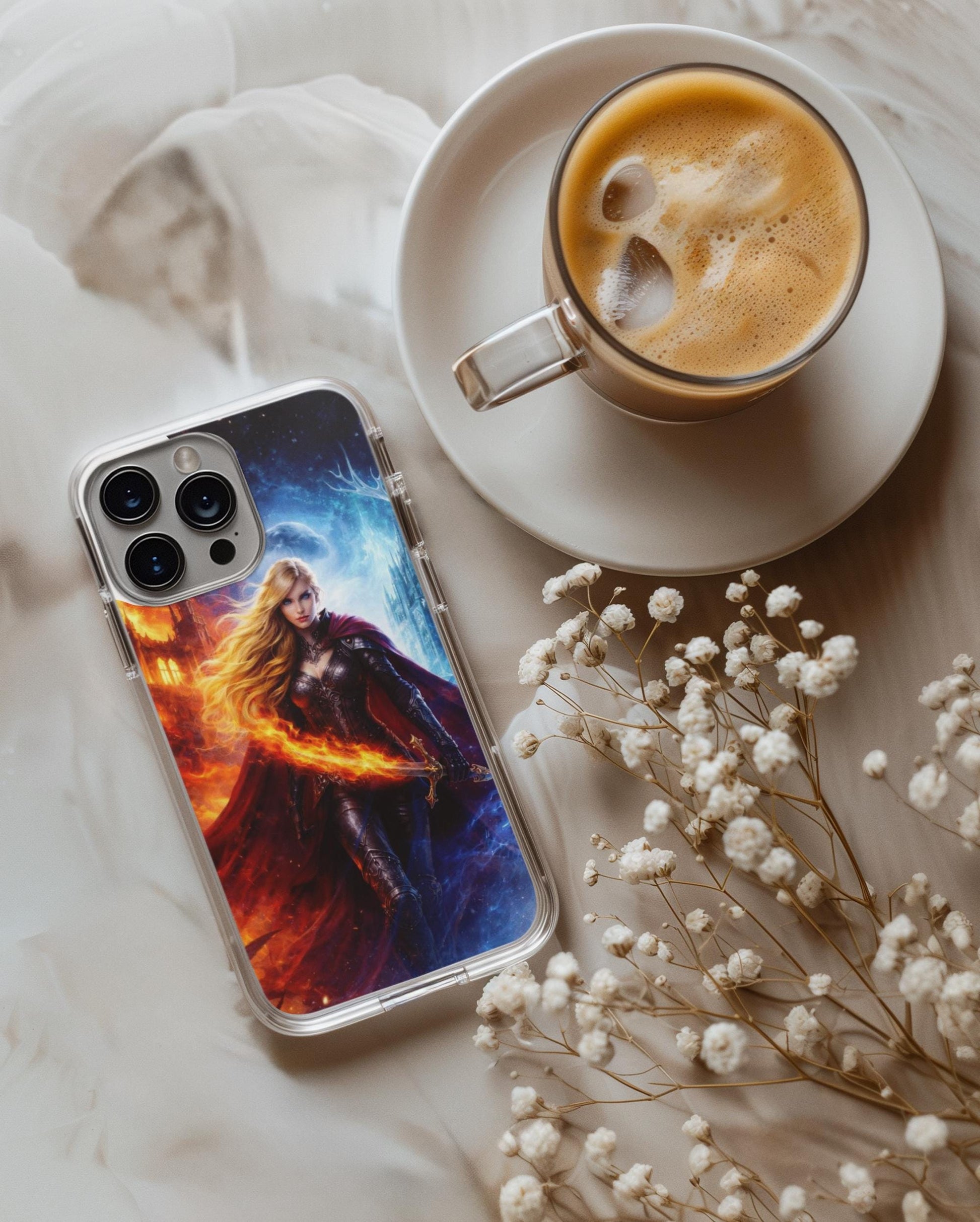 May include: Clear phone case with a fantasy art design featuring a woman with long blonde hair, a red cape, and aClear phone case featuring the fire and ice fantasy warrior goddess art, styled flat-lay on a soft white blanket beside a cup of frothy coffee and sprigs of dried baby's breath. sword, set against a backdrop of fire and ice. A cup of coffee with ice cubes sits on a white saucer. __etsy:7686552472