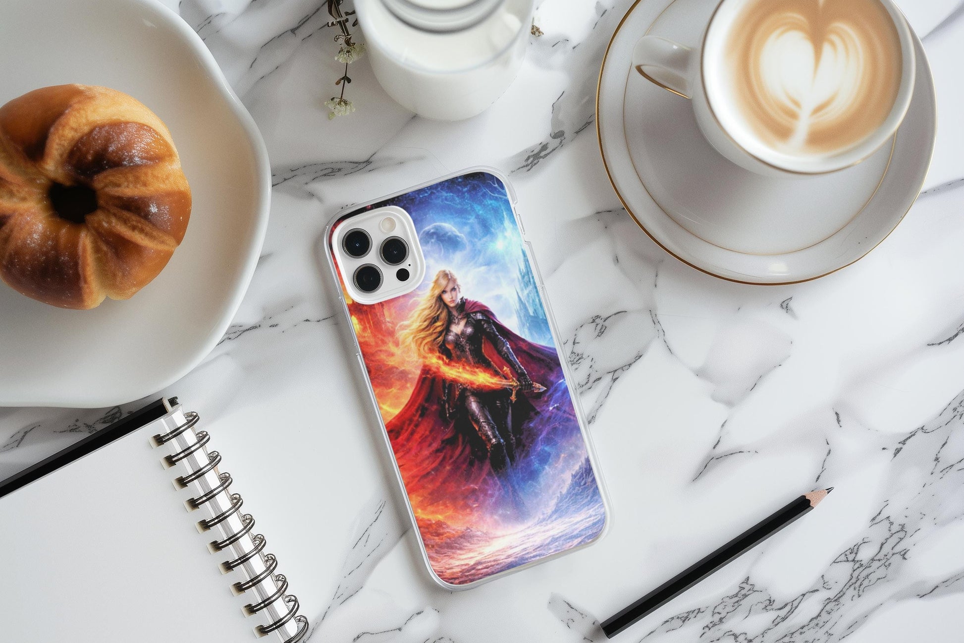 May include: A smartphone case featuring a fantasy illustration of a woman with long blonde hair, wearing a dark oClear phone case with the fire and ice fantasy warrior goddess art on a white marble surface, styled with a heart-topped latte, a pastry on a plate, and an open spiral notebook with a pencil.utfit and red cape, set against a backdrop of fire and ice. The case is on a marble surface, next to a pastry, coffee, and a notebook. __etsy:7734505491