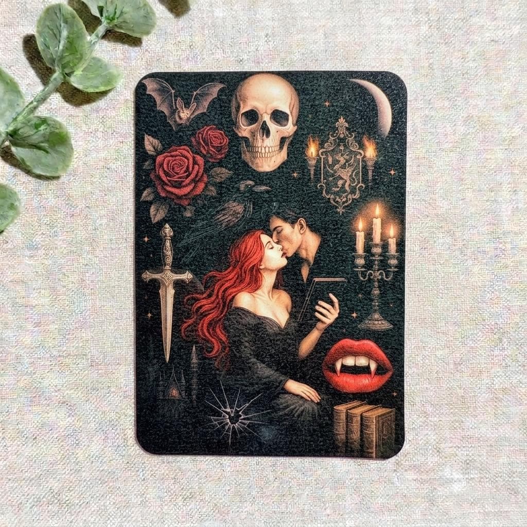 Gothic vampire Kindle insert decal featuring a dark romantasy illustration of a red-haired woman embracing a vampire, with a human skull, red roses, a silver dagger, lit candelabra, bat, crescent moon, and stacked books on a black background. __etsy:8156908489