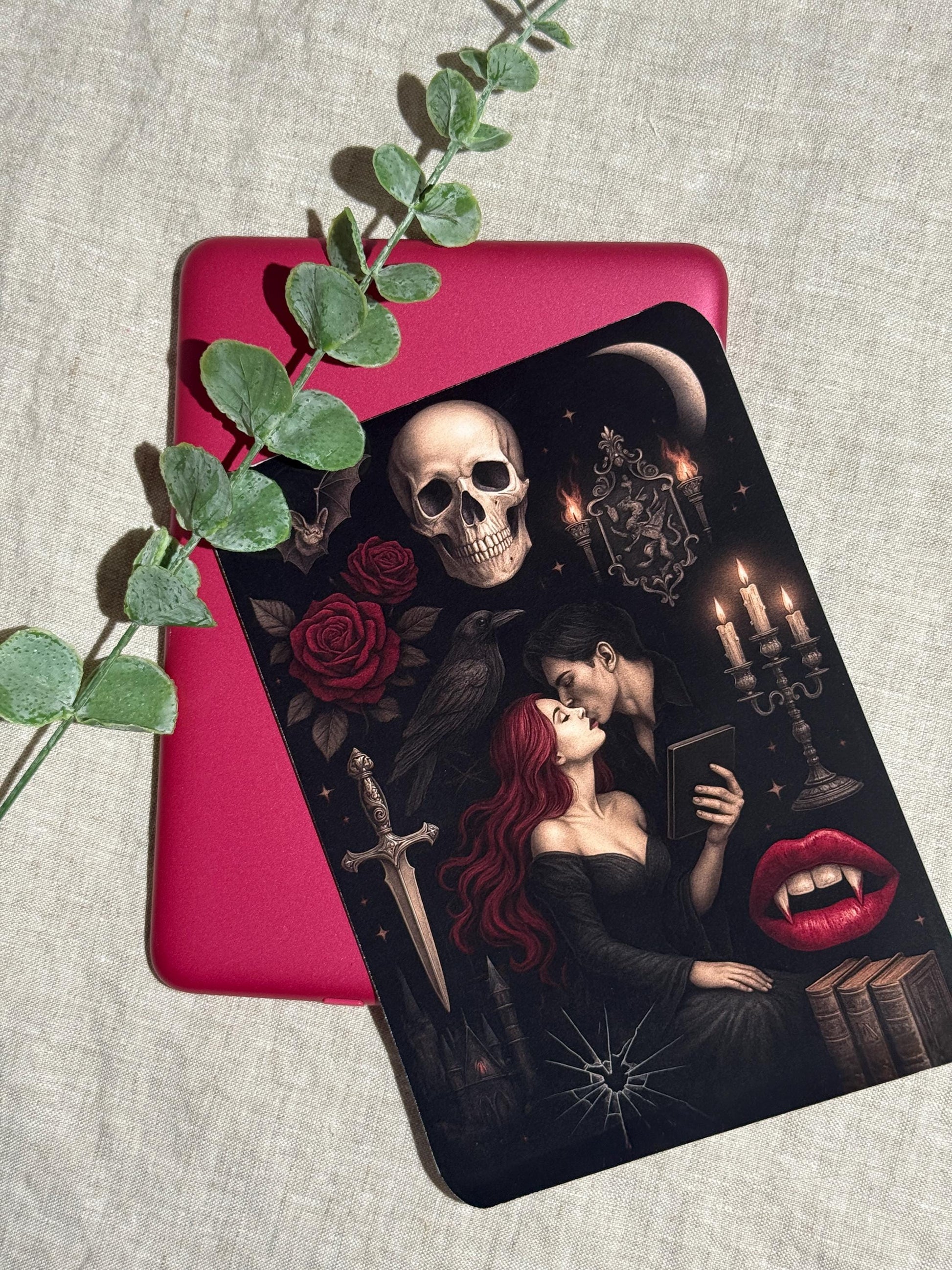 Gothic vampire Kindle insert decal applied to a pink e-reader, shown on a linen background with eucalyptus greenery. The dark romantasy design features a red-haired woman embracing a vampire, a skull, red roses, a raven, a dagger, and lit candelabra. __etsy:8165474921