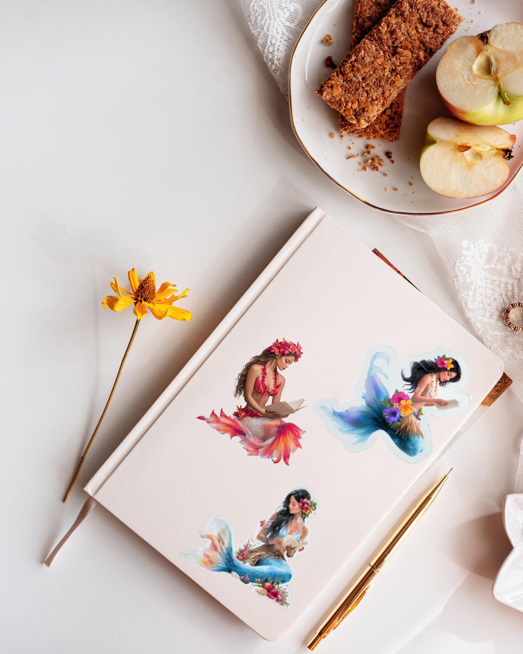 Hawaiian mermaid stickers applied to a cream journal in a flat lay with a yellow flower, gold pen and a plate of granola bars and apple slices __etsy:7732326289