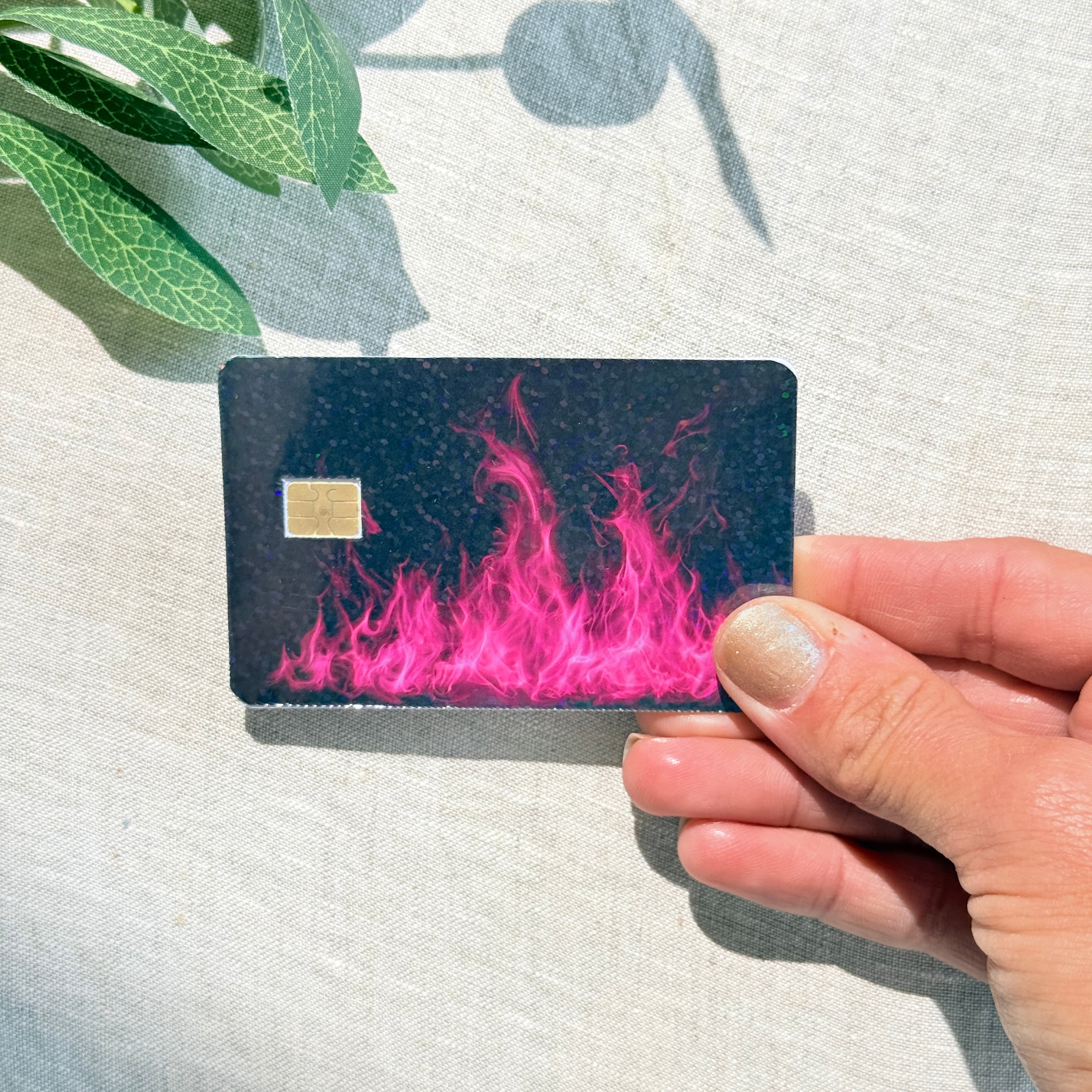 Hand holding a hot pink flame debit card skin in sunlight by The Sticker Era