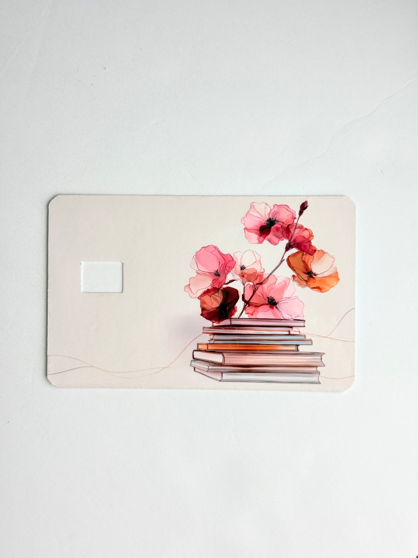 Watercolor art showing a stack of antique books topped with blooming flowers on vinyl card skin."
