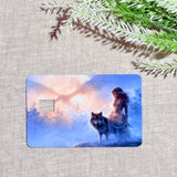 Close-up of the transit-style wolf card with a rectangular swipe cutout, printed with the huntress and gray canine against a snowy blue and orange scene, lying on natural beige linen with a fern branch by The Sticker Era