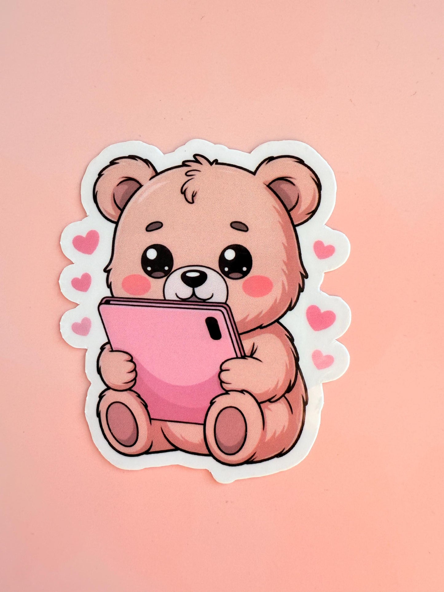 Close-up of a cute, cartoon-style teddy bear sticker with rosy cheeks and sparkling eyes, holding a bright pink smartphone surrounded by floating hearts. The sticker has a matte finish. __etsy:6955453300