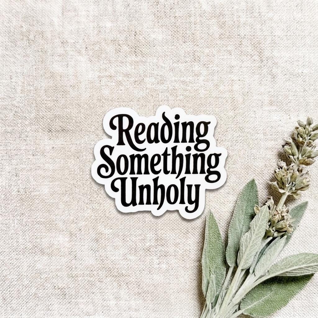 Black and white die-cut vinyl sticker with bold decorative serif lettering reading "Reading Something Unholy," styled for spicy booktok and dark romance readers, shown on a natural linen background with dried sage sprigs. __etsy:8182084031