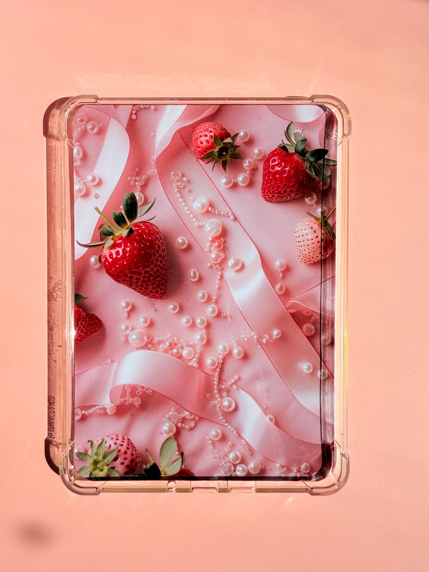 A printed Kindle insert with a coquette aesthetic, featuring red and white strawberries, pink satin ribbon, and scattered pearls on a pink background. The insert has soft lighting and a dreamy, feminine vibe. Photographed on a pastel surface with rounded corners. __etsy:6929546991