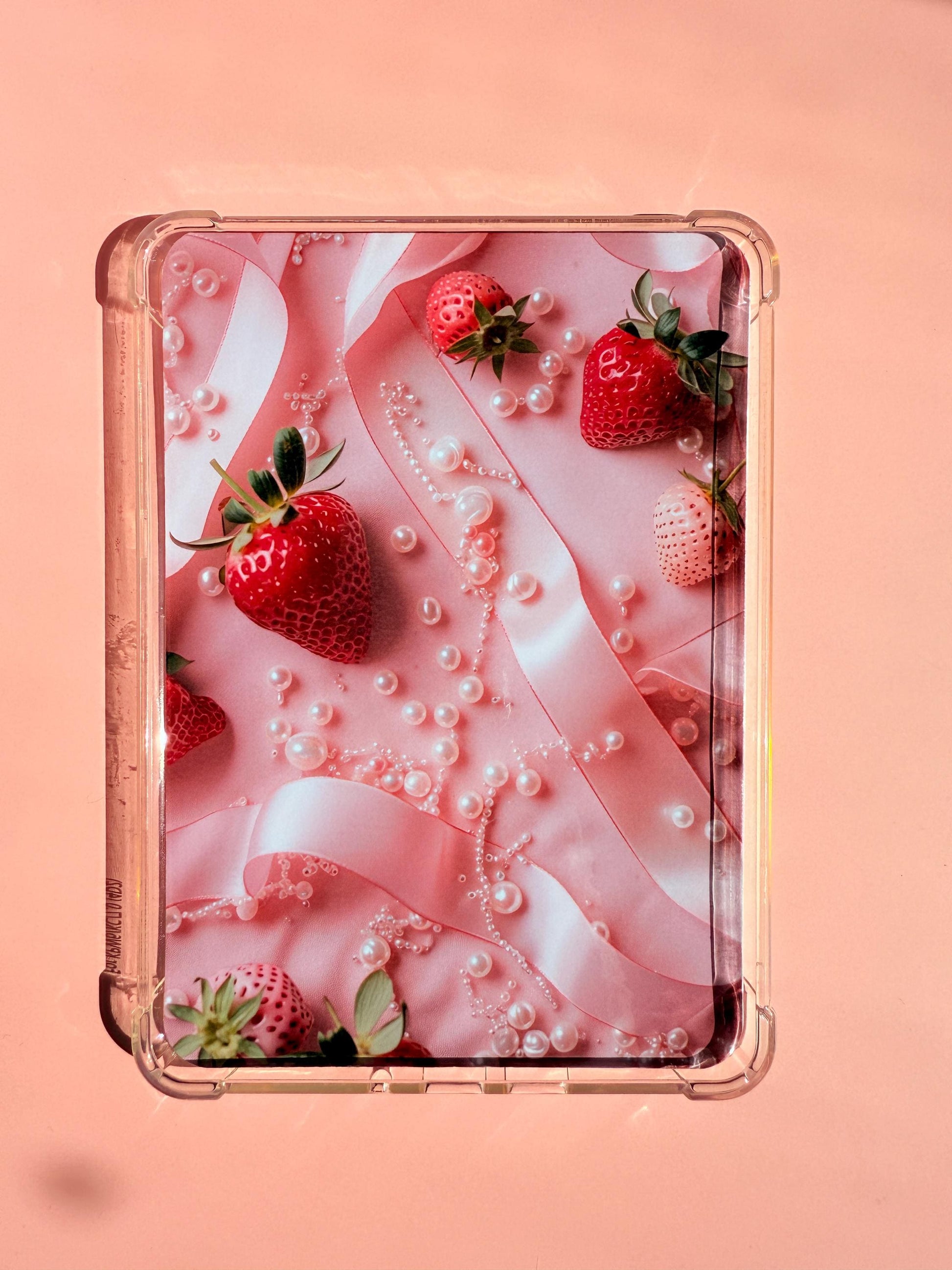 A printed Kindle insert with a coquette aesthetic, featuring red and white strawberries, pink satin ribbon, and scattered pearls on a pink background. The insert has soft lighting and a dreamy, feminine vibe. Photographed on a pastel surface with rounded corners. __etsy:6929546991