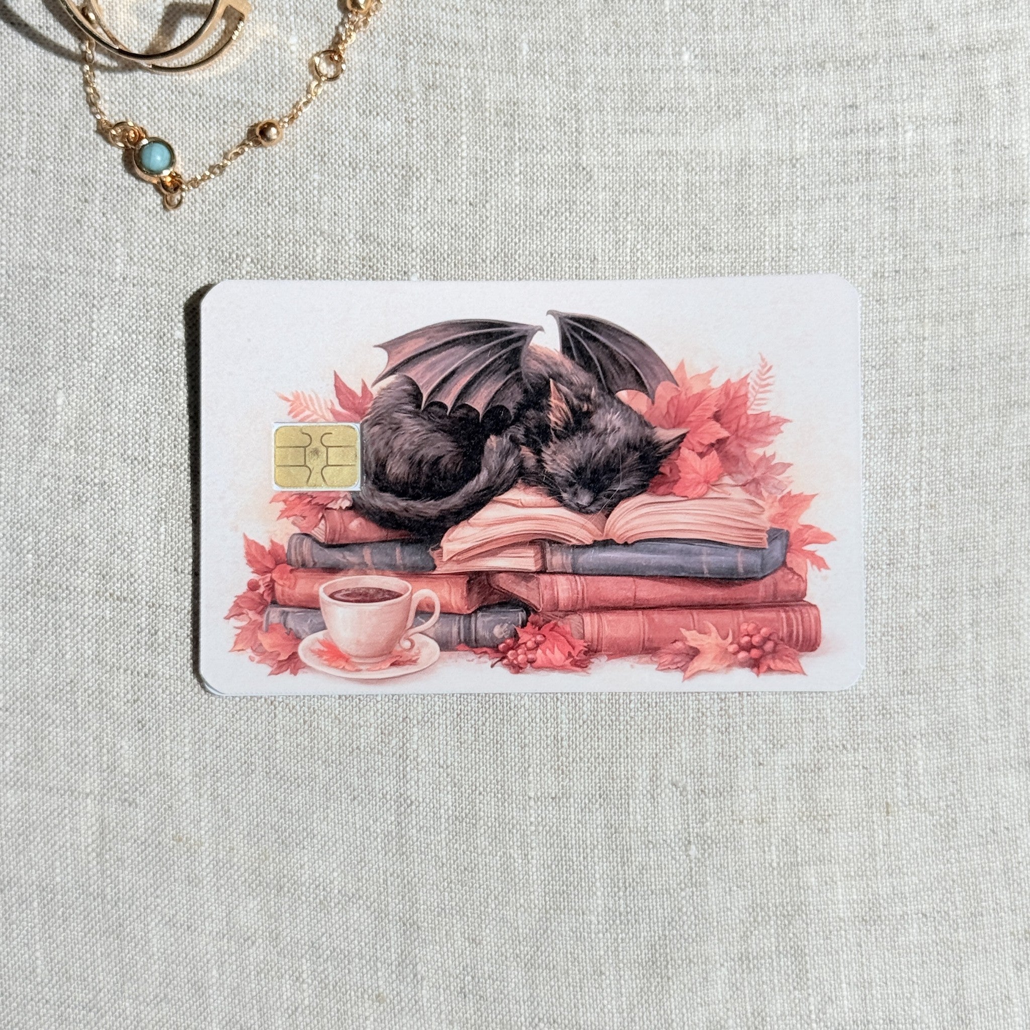 Autumn dragon cat card skin on a debit card, winged black cat asleep on a stack of books