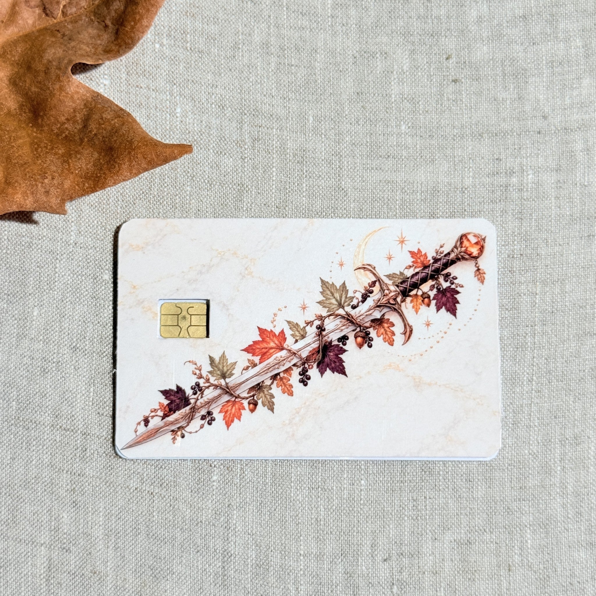 Autumn sword card skin on a debit card, ornate blade wrapped in maple leaves and gold vines