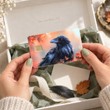 Hands unboxing the autumn raven debit card skin from The Sticker Era packaging