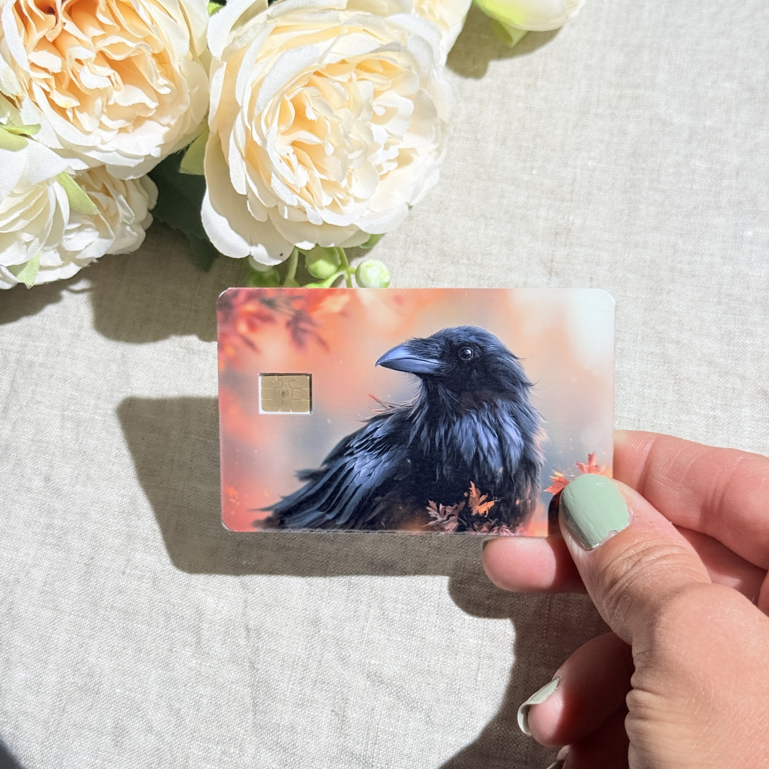 Hand holding the autumn raven debit card skin in sunlight by The Sticker Era