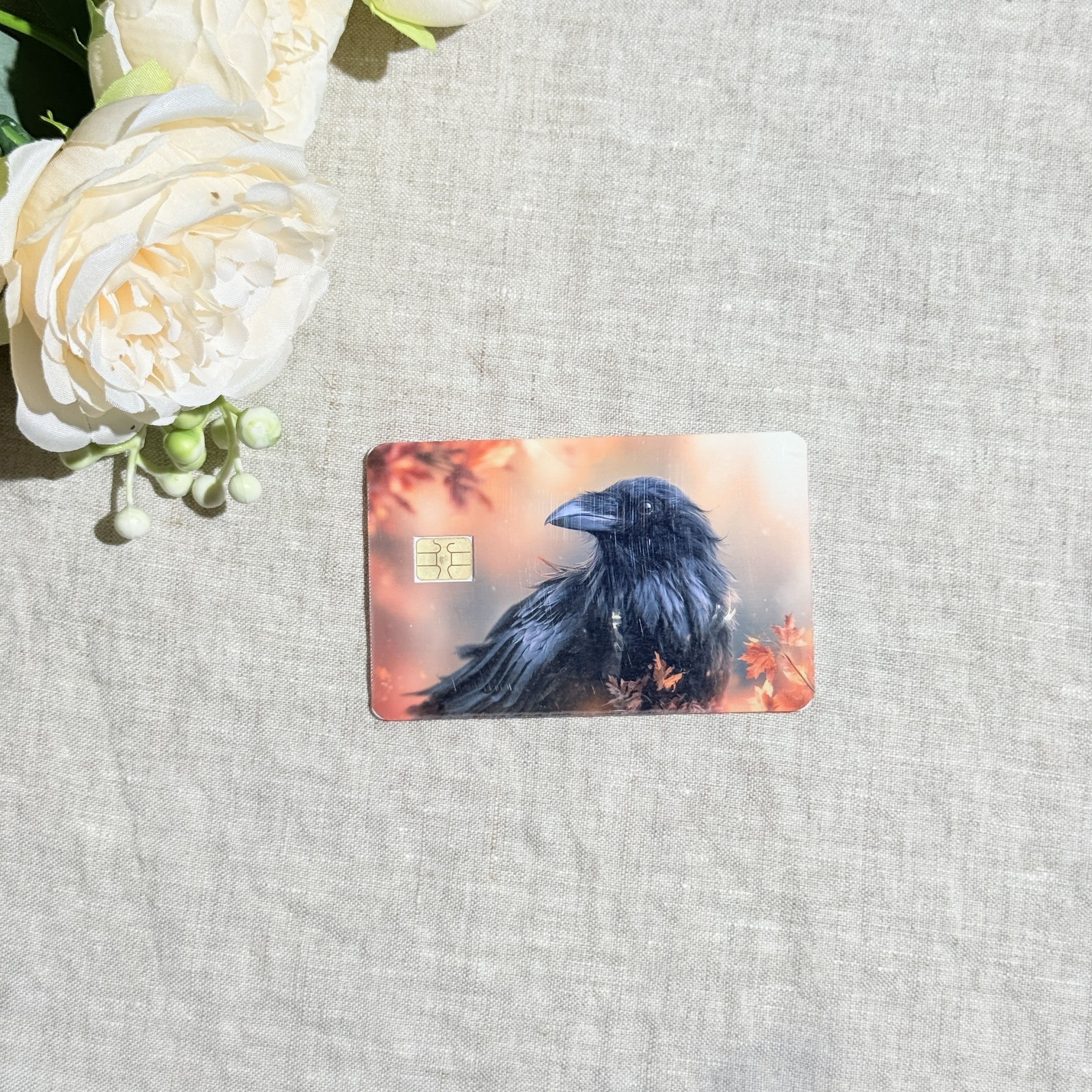 Black raven fall leaves card skin flat lay on cream linen by The Sticker Era