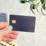 Hand holding the black holographic glitter card skin in sunlight by The Sticker Era