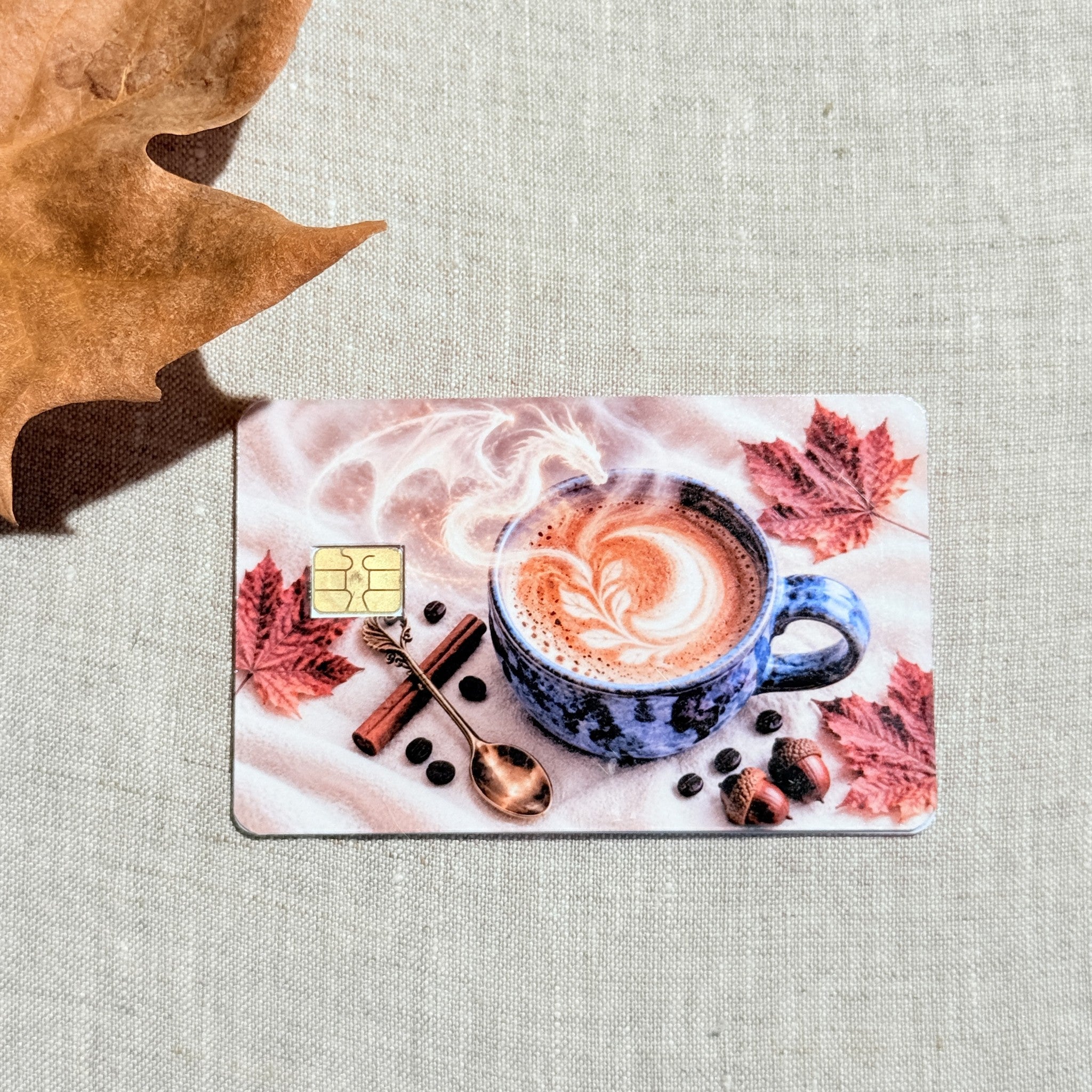 Autumn coffee card skin on a debit card, blue mug with latte art and red maple leaves