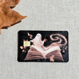 Book ghost card skin on a debit card, a sheet ghost reading with coffee on deep navy
