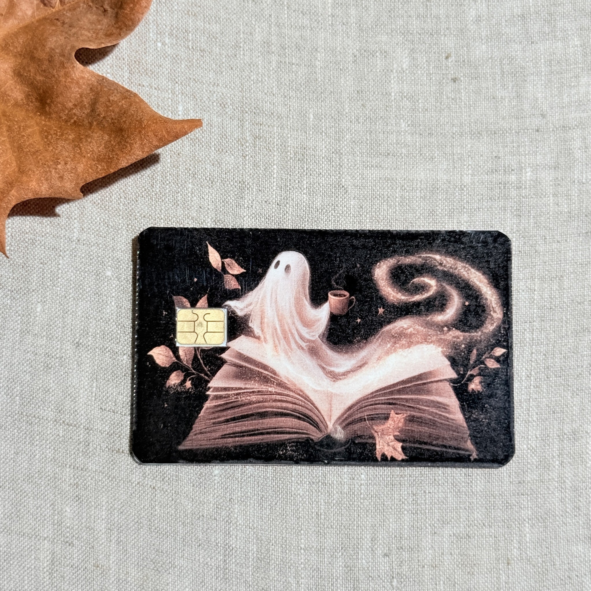 Book ghost card skin on a debit card, a sheet ghost reading with coffee on deep navy