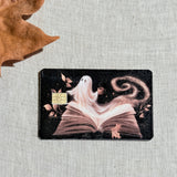 Cozy Halloween ghost debit card sticker shown flat on linen with a fall leaf
