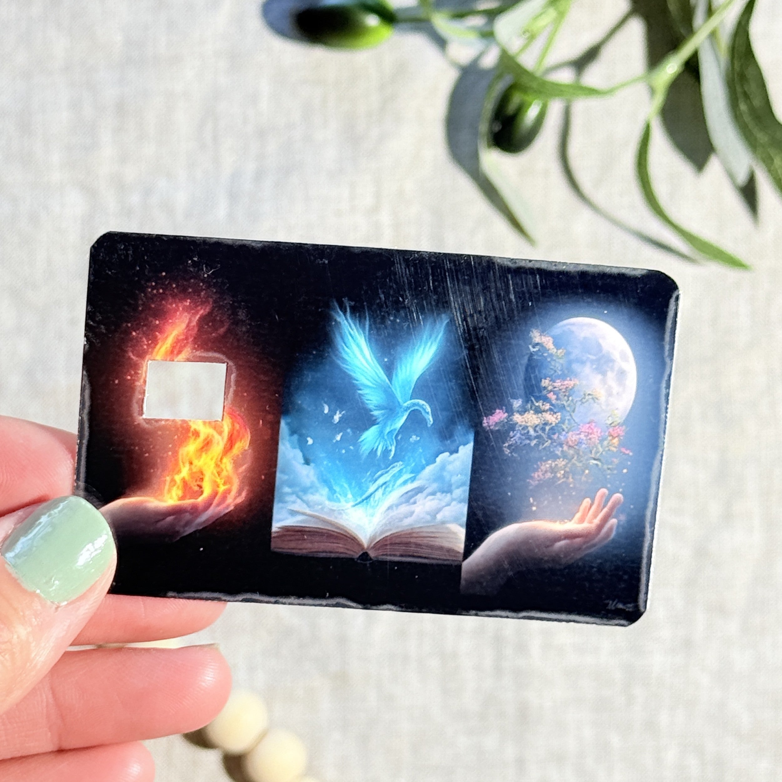 Elemental magic book card skin with fire, blue phoenix and moon panels on a black debit card by The Sticker Era