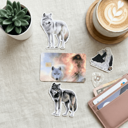 Wolf  and girl on fire debit card sticker, other wolf stickers on a table with a plant, coffee, and wallet.
