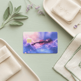 Starry violin card skin on pale green wood between sage leaves and embroidered pouch BY THE STICKER ERA