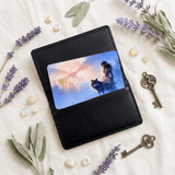 The wolf card tucked into a sleek black leather cardholder wallet on cream cloth, flanked by dried lavender, sage leaves, glossy white pearls, moonstone gems, and antique bronze skeleton keys by The Sticker Era