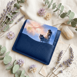 Debit card slotted in a navy blue leather cardholder over an aged treasure map, decorated with dried lavender, eucalyptus branches, pale strawflowers, and a raw moonstone crystal by The Sticker Era