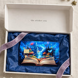 Enchanted storybook card skin in a white gift box with navy tissue and a lavender velvet ribbon by The Sticker Era