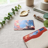 Autumn cozy books card skin beside a tan leather card holder by The Sticker Era