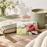 Fluffy cow card skin on a wood table with coffee, a green book and daisies by The Sticker Era
