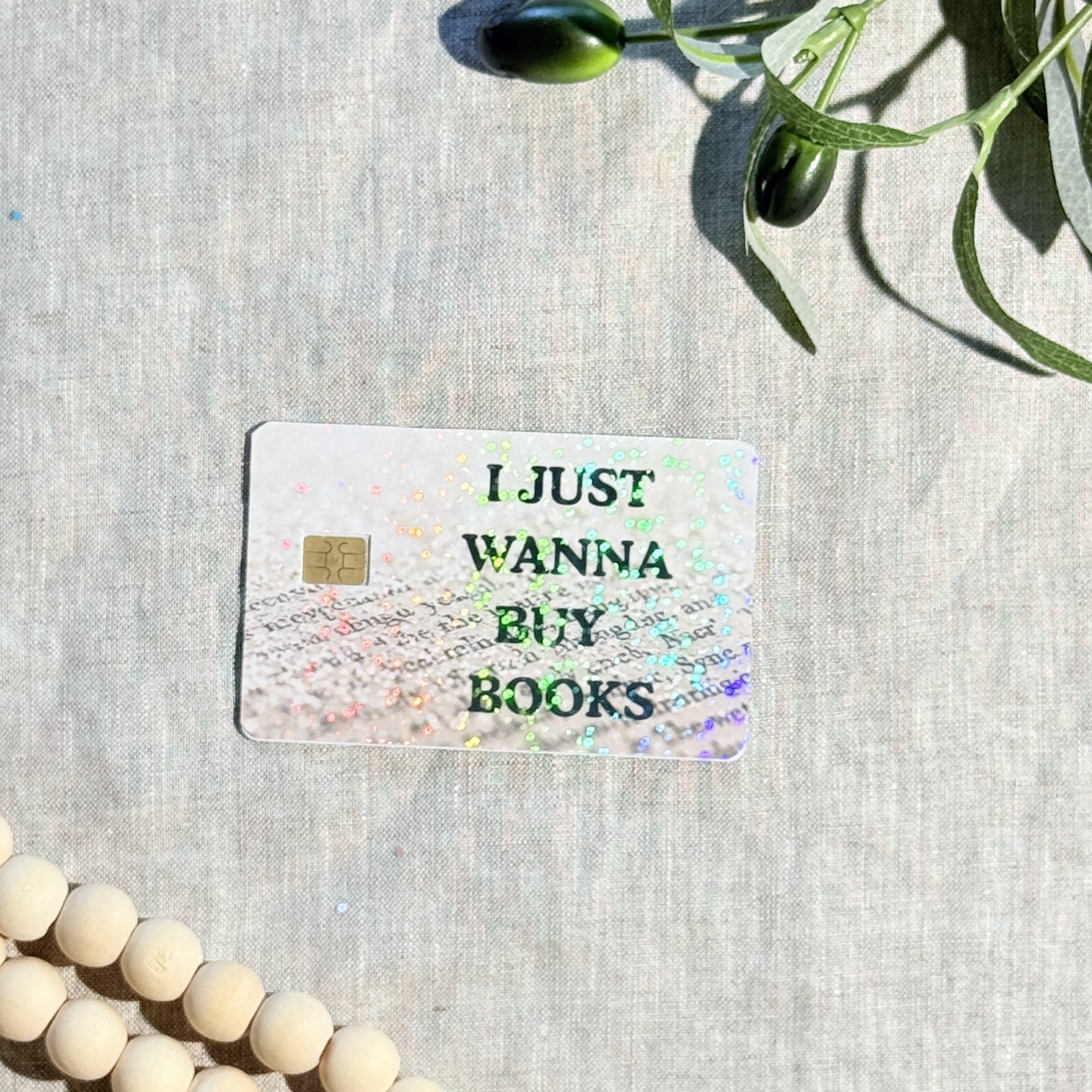 I Just Wanna Buy Books card skin with holographic sparkle over book page text on a debit card by The Sticker Era