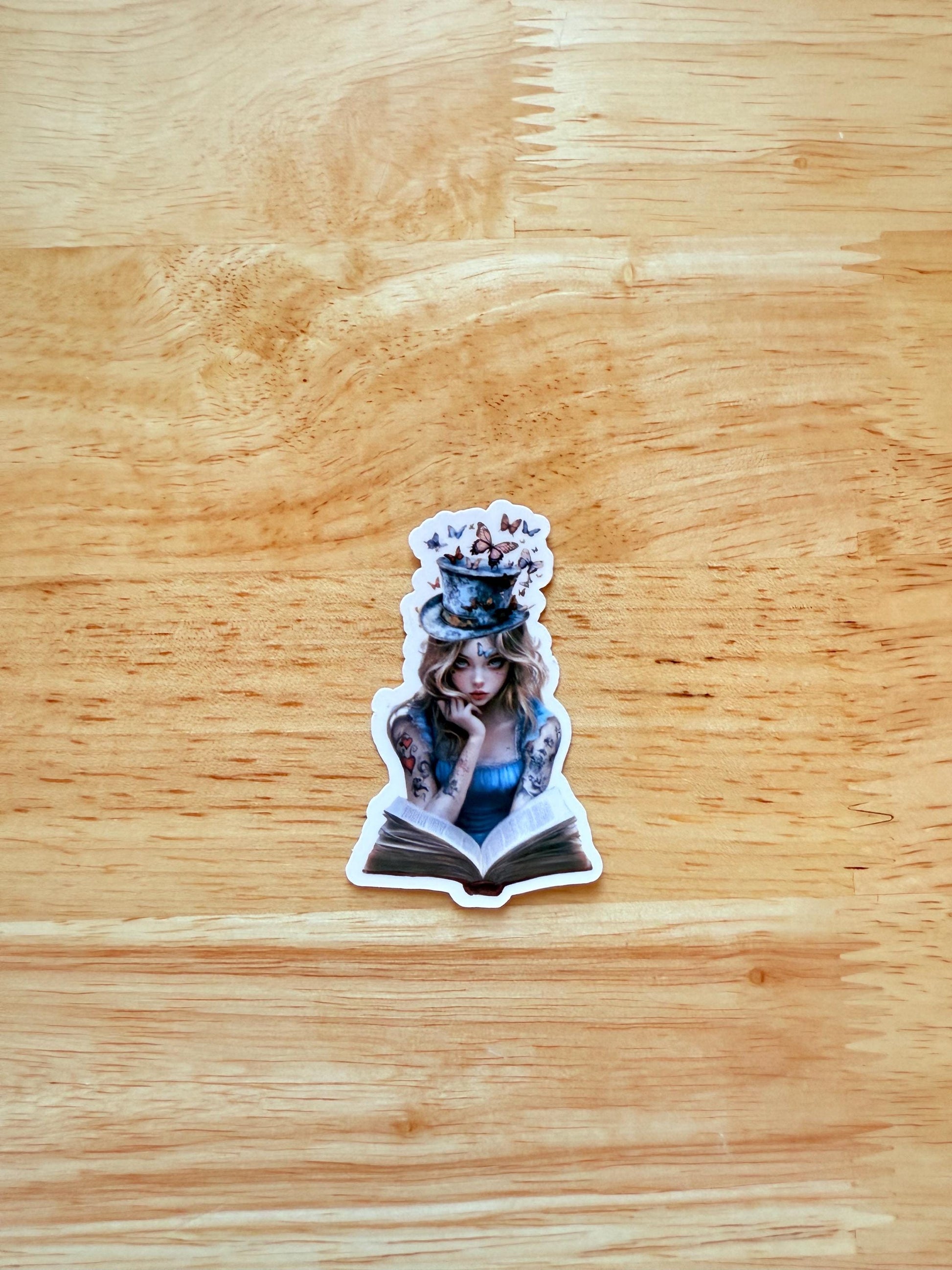Bookish sticker of Alice in Wonderland with modern tattoos, shown reading a book. Designed for fantasy readers and whimsical journal decoration.