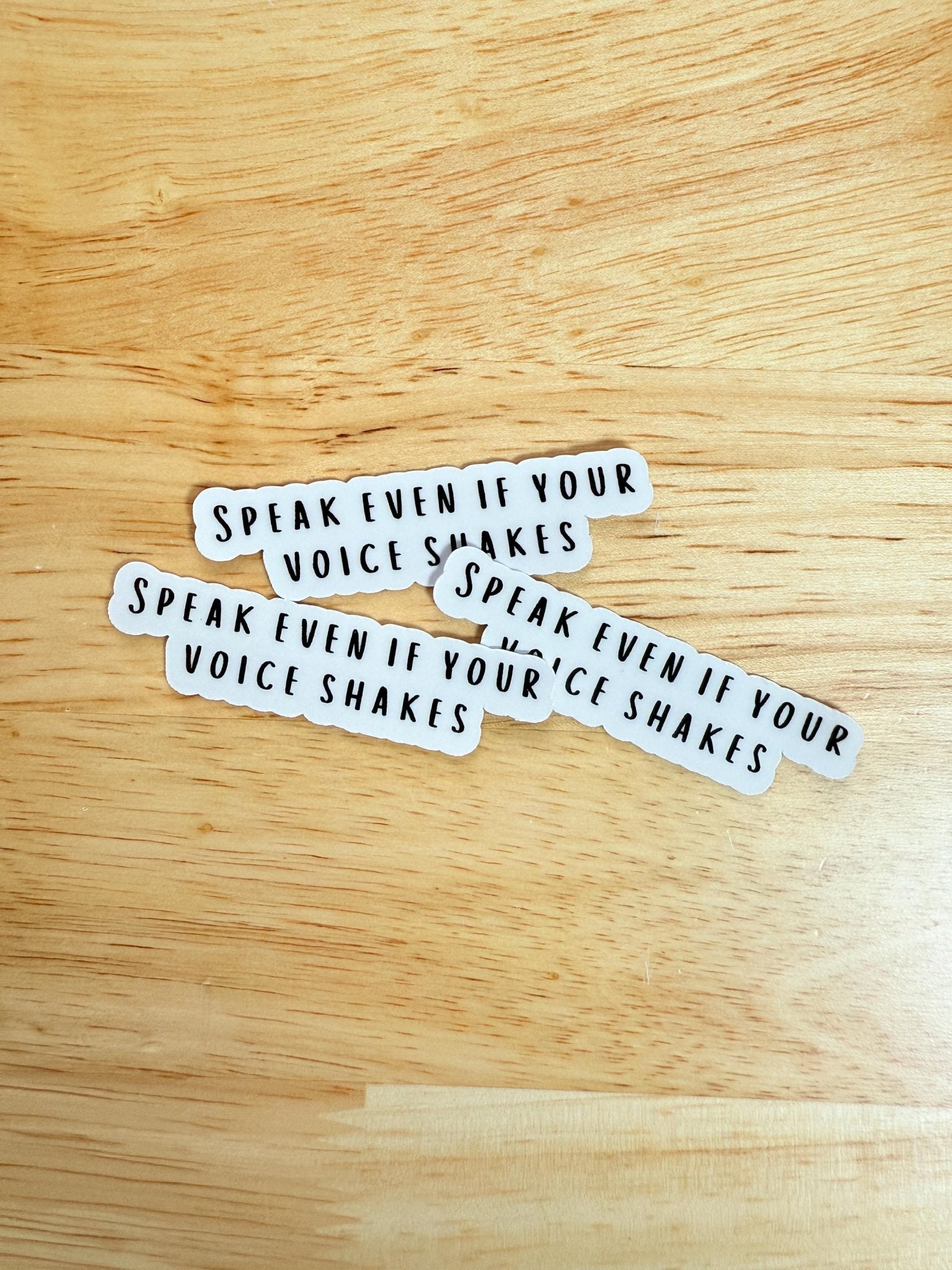 Three "Speak Even If Your Voice Shakes" empowerment stickers on a wooden background