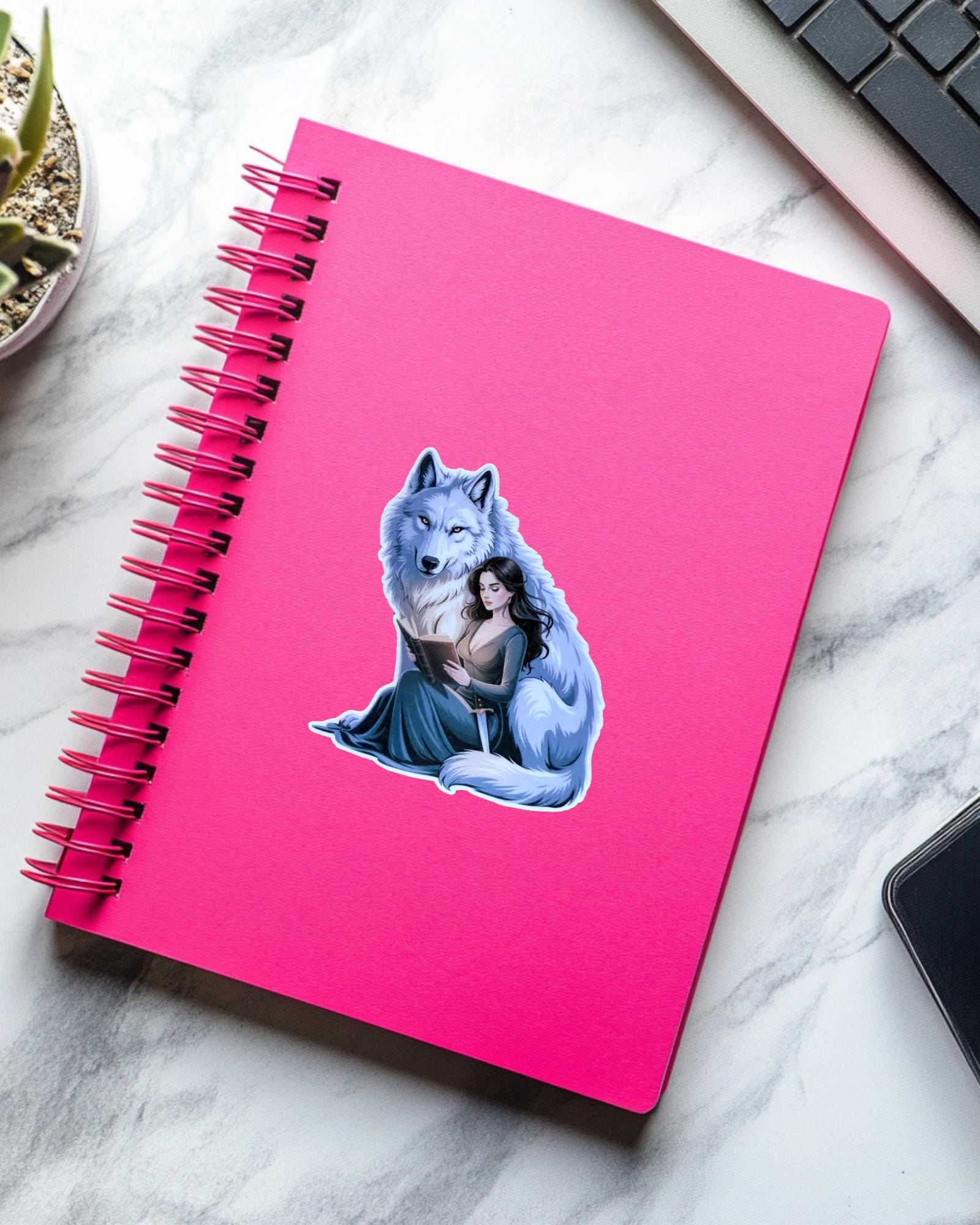 Sticker of a dark-haired fantasy girl character with a sword, inspired by Throne of Glass, placed on a pink notebook. Ideal for fantasy readers, romantasy fans, and bookish journals.