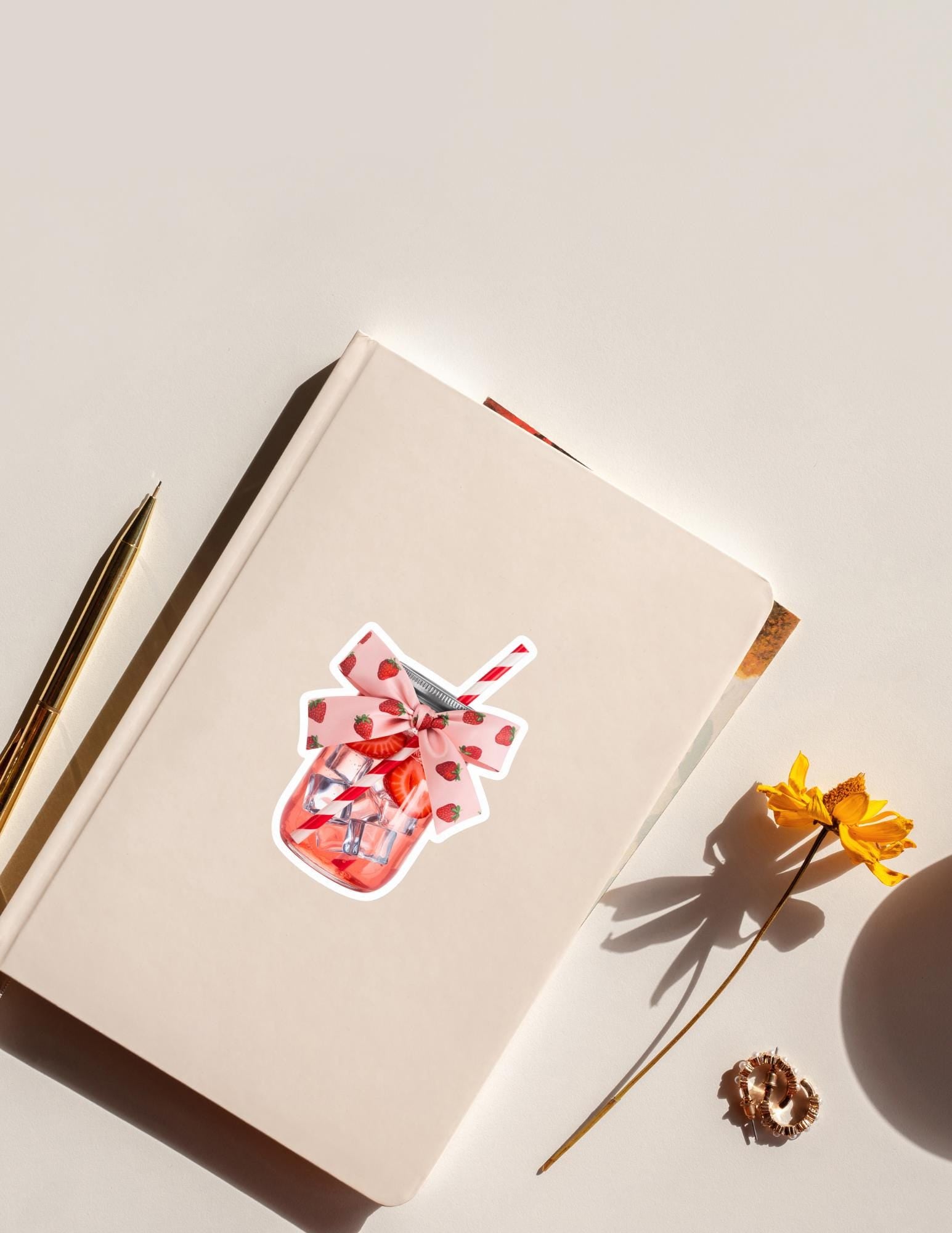 A cute vinyl sticker of a mason jar filled with strawberries, shown on a white notebook. Features a pink ribbon and straw, perfect for summer aesthetics, journaling, or fruit-themed stationery.