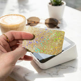  Gold sparkly card skin held in hand beside a coffee cup by The Sticker Era